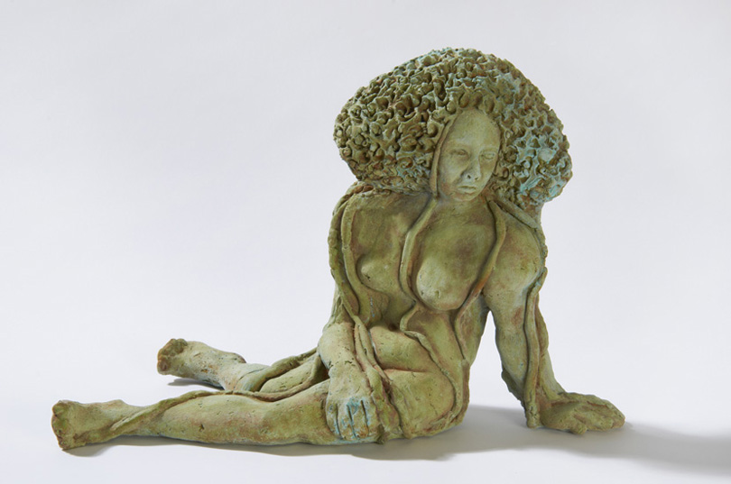 TOPIA, from the Latin topias meaning “ornamental garden”, is a nude figure leaning on one arm and sporting a topiary-like headdress. 